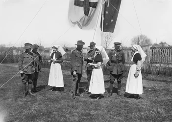 En gruppe uidentificerede betjente, sygeplejersker og mænd fra 3rd Australian Casualty Clearing Station samledes under en flagstang med det australske flag (Australian Blue Ensign) og Røde Kors-flaget