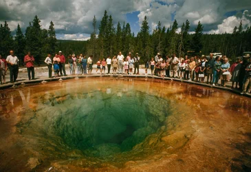Parkgæster samles omkring et blågrønt, blomsterformet termisk bassin. Yellowstone National Park