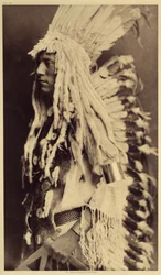 Gammel person, Piegan. Unge mænd går ikke glip af nogen anledning til offentlige festligheder for at tage deres krigerfars tøj på. Foto taget fra bind 6 af encyklopædien udgivet af Edward S. Curtis (1868-1952) om indianerne i Nordamerika, med en forgrund