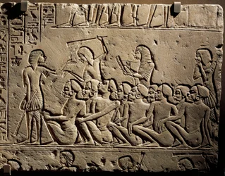 En gruppe sorte fanger omgivet af vagter bevæbnet med køller, mens en skriver udarbejder en rapport, relief fra Horemhebs grav i Saqqara