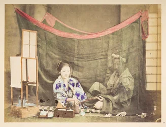 Japansk par i ro og mag, Studio-tableau af en ung japansk kvinde, siddende med telavningshinder omkring sig, og rækker en pibe til en mandsfigur, der sidder bag hende, skærmet af et linnedmyggenet,   Fotograf: Ukendt  Lucas samling: