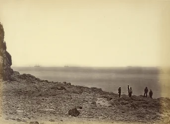 [Udsigt til kysten med skibe i horisonten og fem personer, der står på stranden].