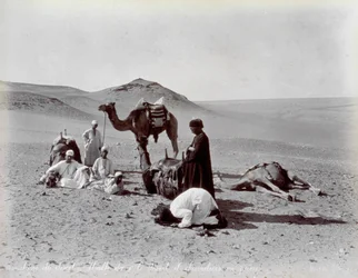 Egyptiske camelere under en pause i ørkenen. I forgrunden ser to medlemmer af den lille gruppe ud til at bede.