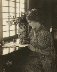 Mary Pickford, iført kimono, skriver ved et skrivebord, ca. 1918 (s/h-foto)