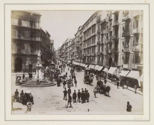 Udsigt over Via Roma i Napoli med en statue, butikker, hestevogne og forbipasserende