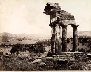 Udsigt over de resterende fire søjler, der understøtter en entablatur af Castor- og Pollux-templet i Valle dei Templi, Agrigento. Et panorama af byen er synligt i baggrunden