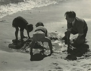 Tre børn leger med sand på stranden.