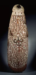 Ovalt Asmat-skjold, udskåret i relief med rullende ornament med meget stiliserede figurer, flettede kvaster til kanten (træ, raffia og fjer)