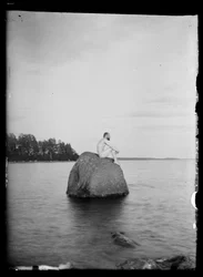 Hugo Simberg sidder på en klippe med Essaari og Suonionsaari i baggrunden.