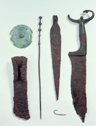 Oppefra og ned: Kniv, spydspids, fiskekrog, tøjklemme, bælteskive og økse, alle fundet i mandegrave i Hallstatt, jernalderen