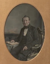 Siddende mand peger på en passage i en åben bog, 1850