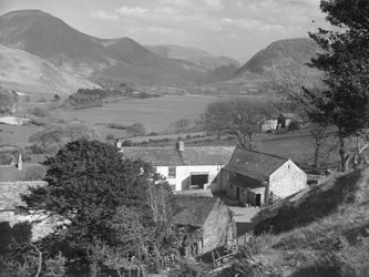 En udsigt over noget, der ser ud til at være en gård i forgrunden og en sø og fjelde i baggrunden.