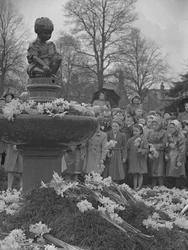 Børn lægger klaser af påskeliljer på springvand med statue på toppen