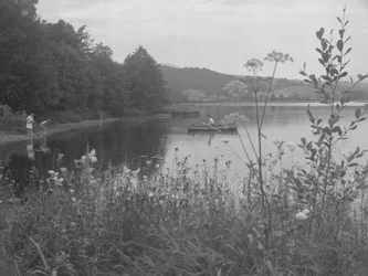 Mand fisker i en båd på Estwaite Water og to piger i vandkanten
