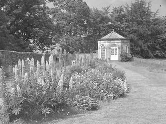 Sommerhus eller folly i have med græsplæne og blomsterbede