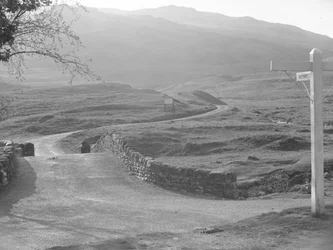 Udsigt til vejen, der går over Hardknott Pass med et skilt, der peger i retning af Hardknott