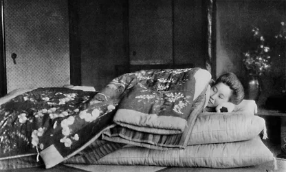Saki, husholdersken sover på en madras med hård pude under en quiltet kimono, c1900, 1921
