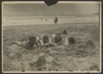 [Børn, der ligger i sandet på stranden]