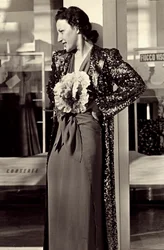 Model i aftenkjole skabt af det italienske couture-hus "Dragoni". Artiklen er pyntet med en imponerende blomst og suppleret med en overfrakke med pailletter. (s/h foto)