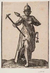 Stående hjelmklædt soldat, frontalt set; i h. hånd en stridshammer, i v. hånd en stridskølle, bageste ben og fod forvredet i forhold til forreste; ved v. side et sværd
