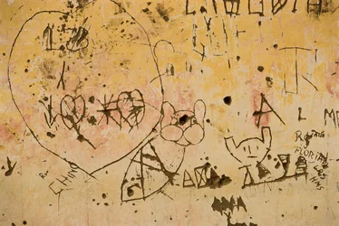 Grafitti ætset ind i en gammel udvendig gipsvæg.