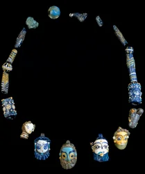 Halskæde i glaspasta med vedhæng, der forestiller skæggede hoveder, oprindeligt fra Olbia, nu konserveret på Cagliari National Archeological Museum