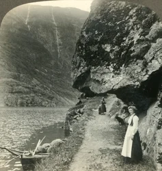 Hvor vejen kryber under de fremspringende klipper ved vandet i Nerofjorden, Norge, c1905.