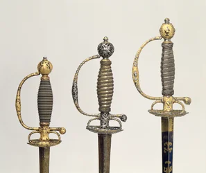 Hilt af tre franske sværd: et af stål, blåt og overtrukket med mønstre i jaget guld, ca. 1730; en af stål gennemboret og mejslet og slebet af matteret guld, c.1760; en af mejslet stål, gr