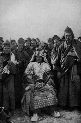 Tibet. Tryllekunstner i fuld påklædning og en beundrende flok munke. 1920