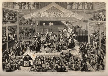 En scene i det japanske teater i Yokohama med tre gallerier til modtagelse af tilskuere; skuespillerne spiller på en høj scene, hver akkompagneret af en mand, der holder en lang pind for enden af, hvis stearinlys holdes; under forestillingen er det ikke un