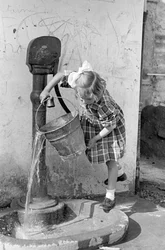 Lille pige tømmer en spand vand i et pumpefontæne, 9. maj 1939 (s/h-foto)