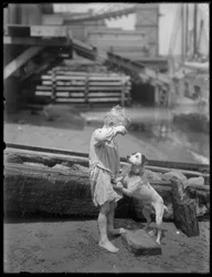 Barfodet dreng, muligvis William Gray Hassler, leger med hund ved bredden af en flod eller sø, New York, ca. 1910