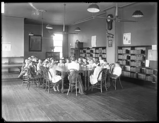 Børn lytter til en kvinde i læsesalen i en uidentificeret filial af Queens Borough Public Library, ca. 1910