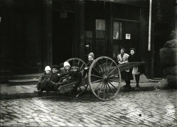 Gruppe af børn i vogn, med pige og kvinde bagved, ca. 1910-21