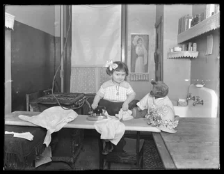 Uidentificeret lille pige demonstrerer brugen af et elektrisk strygejern, ca. 1913-14