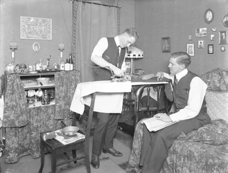 Uidentificeret mand, der demonstrerer brugen af et elektrisk strygejern, overvåget af en anden mand, ca. 1913-14